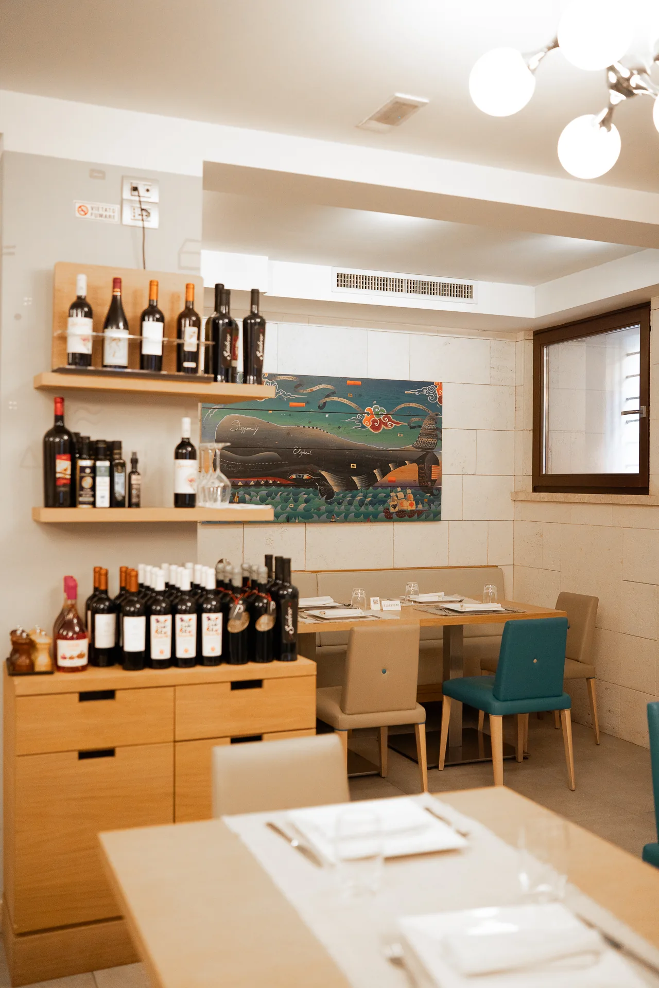Sala del ristorante con tavoli apparecchiati, bottiglie e un dipinto di una balena.